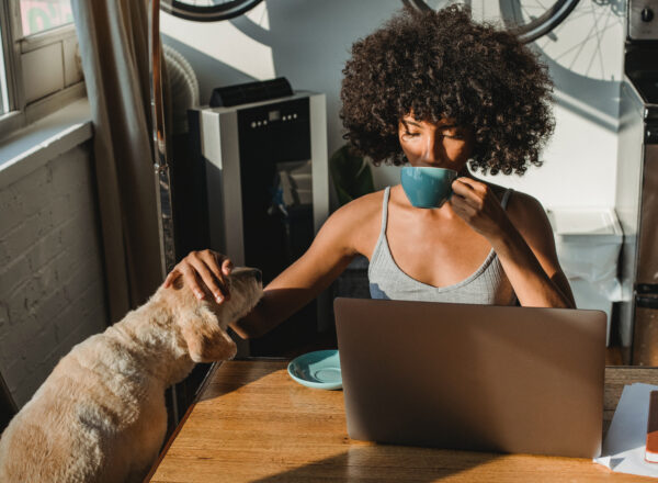 woman drinking from a blue cup at her laptop while petting her dog