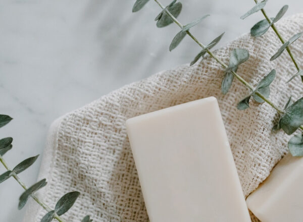 a white piece of soap on top of a white, waffle-patterned wash cloth and a piece of eucalyptus on a white table