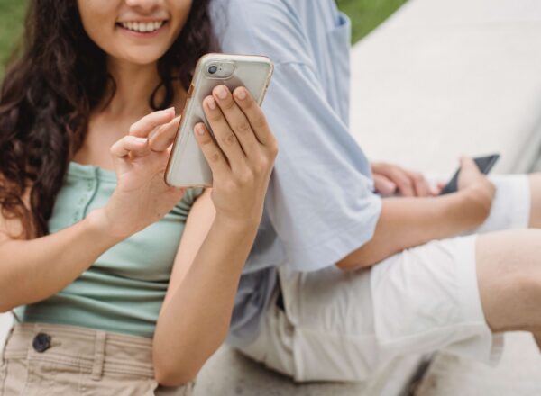 Woman holding a phone and leaning her back on a man, who is also holding a phone.