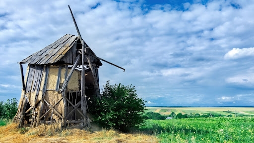 An old windmill situated in a farm, against the backdrop of a blue sky and some clouds.