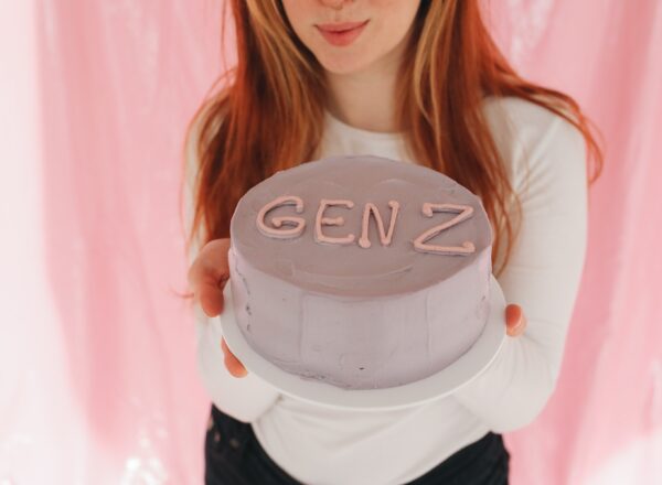 A girl holding out a minimalist cake with "Gen Z" written on the top in icing.